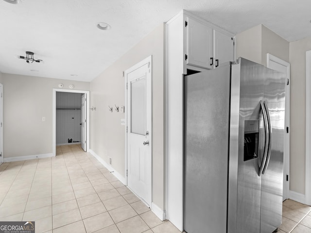 kitchen with white cabinets, light tile patterned flooring, stainless steel refrigerator with ice dispenser, and baseboards