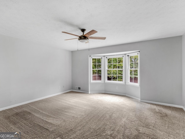 carpeted empty room featuring ceiling fan, a textured ceiling, visible vents, and baseboards