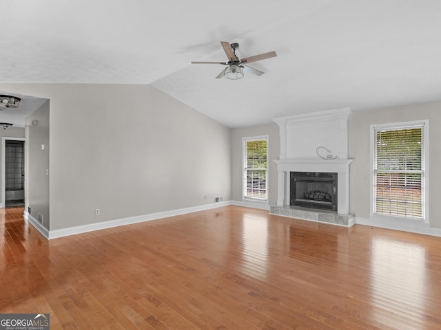 unfurnished living room with light wood-style flooring, a ceiling fan, vaulted ceiling, a tile fireplace, and baseboards