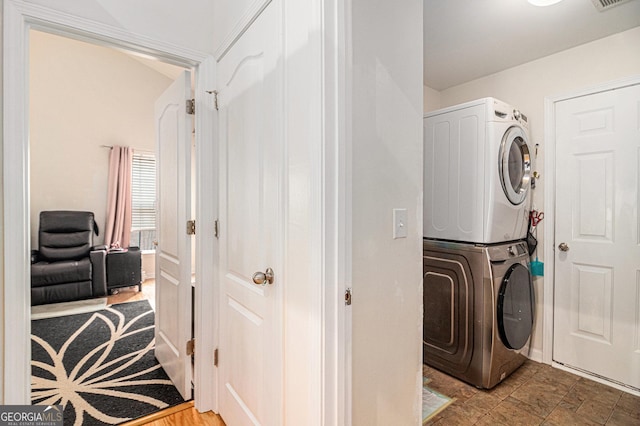 clothes washing area featuring stacked washer and dryer, laundry area, visible vents, and stone finish flooring