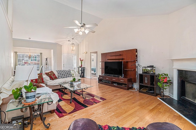 living area featuring high vaulted ceiling, a high end fireplace, ceiling fan with notable chandelier, and wood finished floors