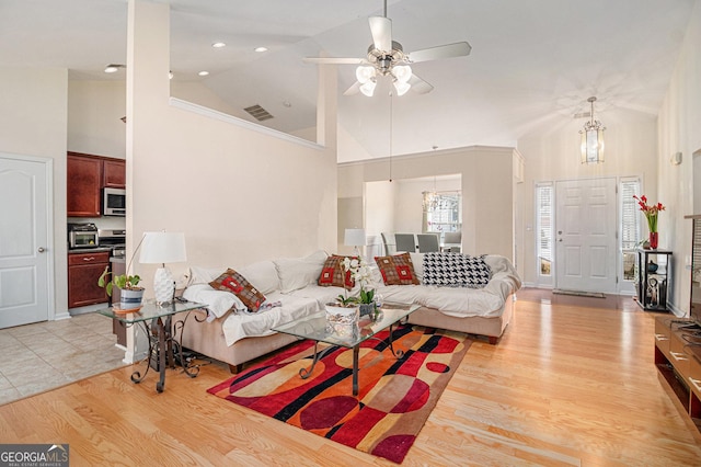 living area with ceiling fan with notable chandelier, high vaulted ceiling, light wood-type flooring, and visible vents