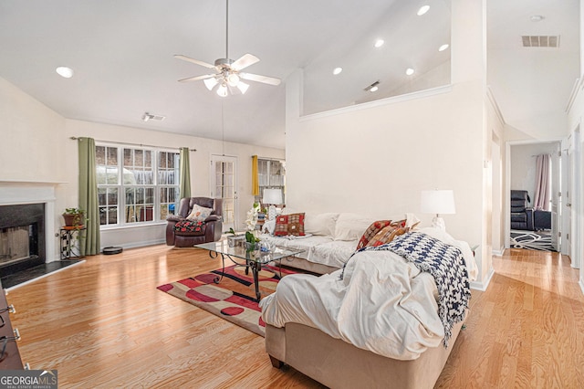 living area with a fireplace, visible vents, light wood-style floors, ceiling fan, and high vaulted ceiling