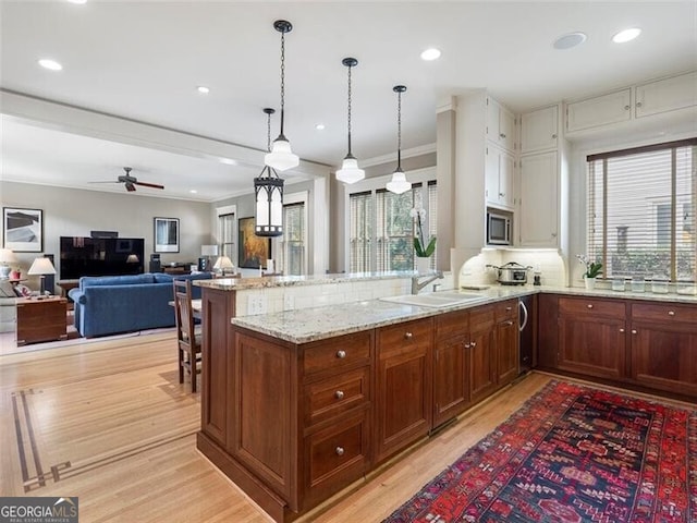 kitchen with light stone counters, stainless steel microwave, light wood-style floors, a sink, and a peninsula