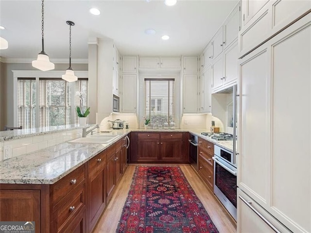 kitchen featuring light stone counters, stainless steel appliances, light wood-style floors, a sink, and a peninsula