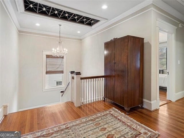 hall with wood finished floors, an upstairs landing, baseboards, ornamental molding, and an inviting chandelier