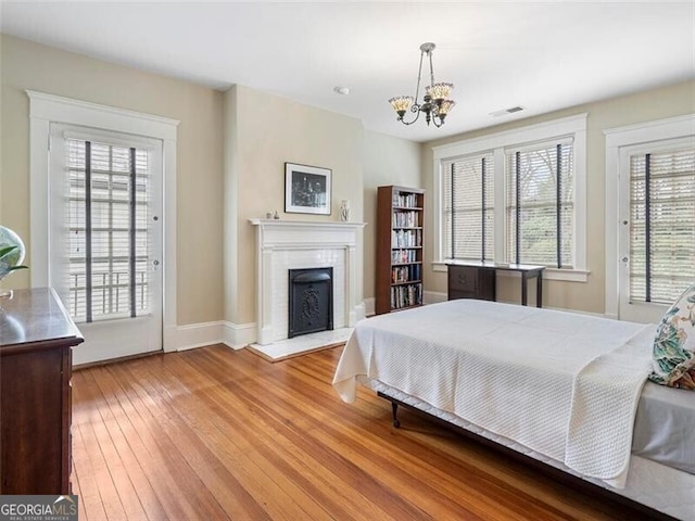 bedroom with access to exterior, a fireplace, wood-type flooring, visible vents, and an inviting chandelier