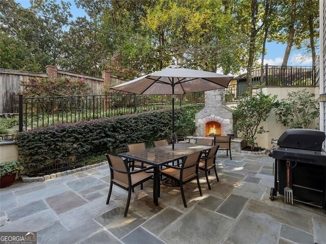 view of patio with fence, an outdoor stone fireplace, grilling area, and outdoor dining space