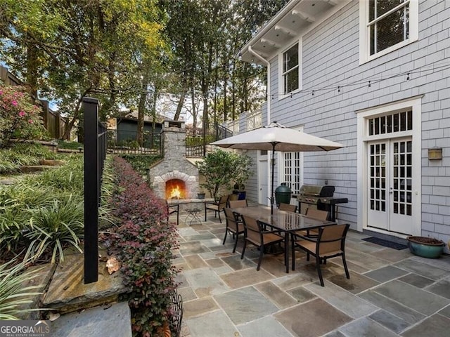 view of patio / terrace with an outdoor stone fireplace, area for grilling, fence, french doors, and outdoor dining space