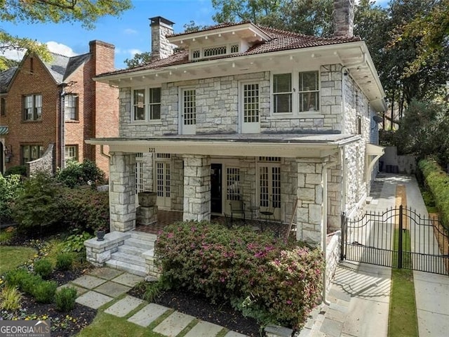 traditional style home featuring stone siding, a gate, and a chimney