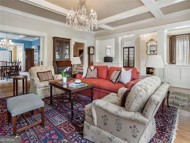 living area featuring a warm lit fireplace, coffered ceiling, a notable chandelier, and beamed ceiling