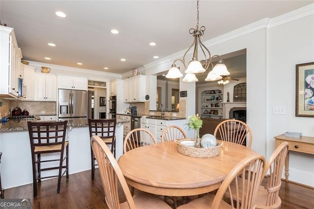 dining area with a fireplace, dark wood-style flooring, ceiling fan with notable chandelier, and crown molding