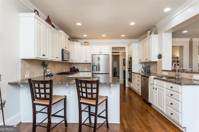 kitchen featuring a sink, appliances with stainless steel finishes, dark stone counters, and a peninsula