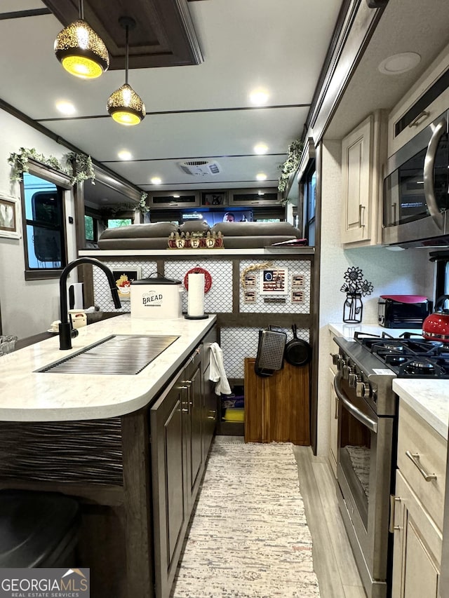 kitchen featuring light wood-style flooring, stainless steel appliances, light countertops, pendant lighting, and a sink