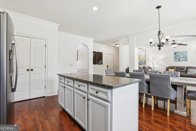 kitchen with arched walkways, open floor plan, a kitchen island, dark stone counters, and stainless steel fridge