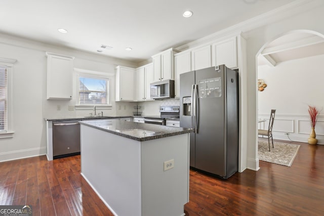 kitchen with white cabinets, dark stone counters, a center island, stainless steel appliances, and a sink