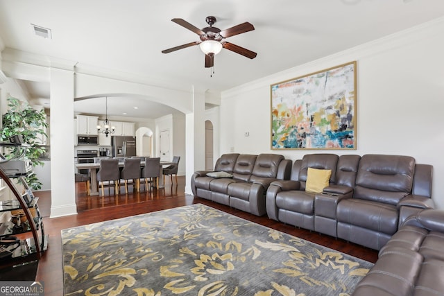 living area featuring arched walkways, crown molding, dark wood finished floors, visible vents, and ceiling fan with notable chandelier