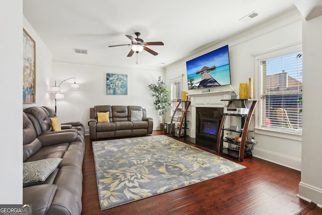 living room featuring visible vents, ceiling fan, a glass covered fireplace, and dark wood finished floors