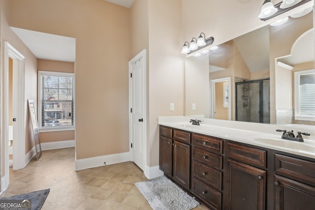 bathroom with double vanity, a stall shower, baseboards, and a sink