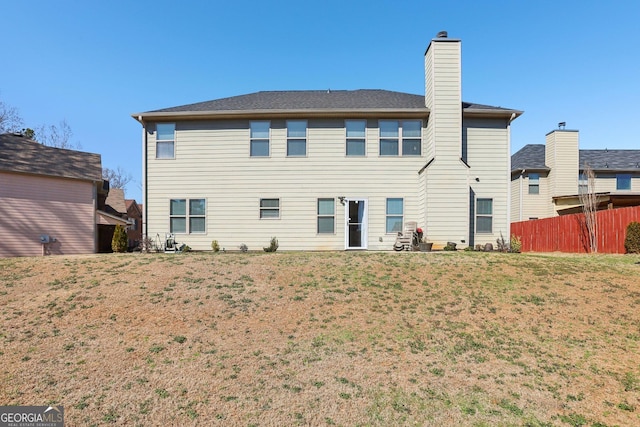 back of property with a lawn, a chimney, and fence