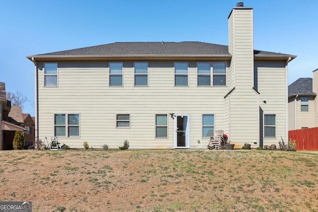 rear view of house with a chimney, fence, and a yard