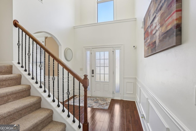 foyer entrance with a towering ceiling, hardwood / wood-style flooring, a decorative wall, and wainscoting