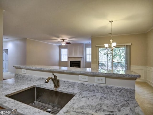 kitchen featuring light stone counters, open floor plan, hanging light fixtures, a decorative wall, and a sink