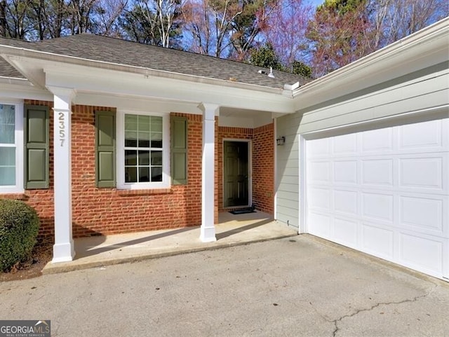 entrance to property with brick siding, a shingled roof, a porch, a garage, and driveway