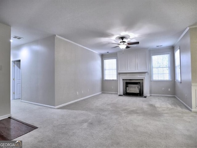 unfurnished living room featuring light carpet, visible vents, baseboards, a fireplace with flush hearth, and ornamental molding