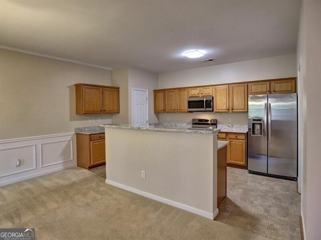 kitchen featuring light stone counters, a center island, brown cabinets, stainless steel appliances, and light carpet