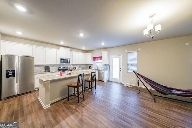 kitchen featuring a center island with sink, white cabinets, light stone counters, decorative light fixtures, and stainless steel appliances