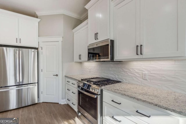 kitchen featuring decorative backsplash, appliances with stainless steel finishes, ornamental molding, white cabinetry, and light stone countertops