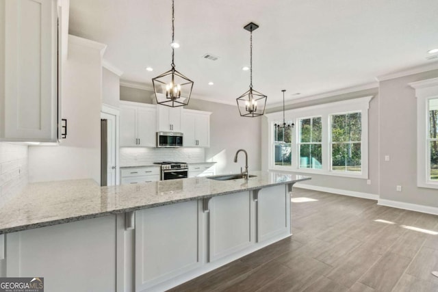 kitchen featuring stainless steel appliances, white cabinets, a sink, and decorative light fixtures