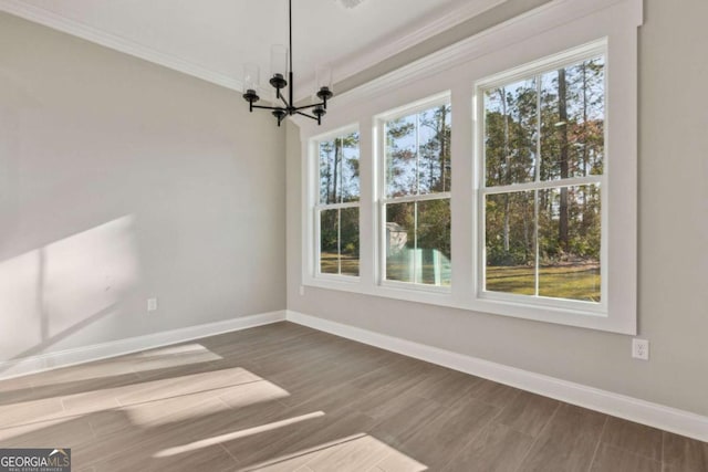 unfurnished dining area featuring wood finished floors, crown molding, baseboards, and an inviting chandelier