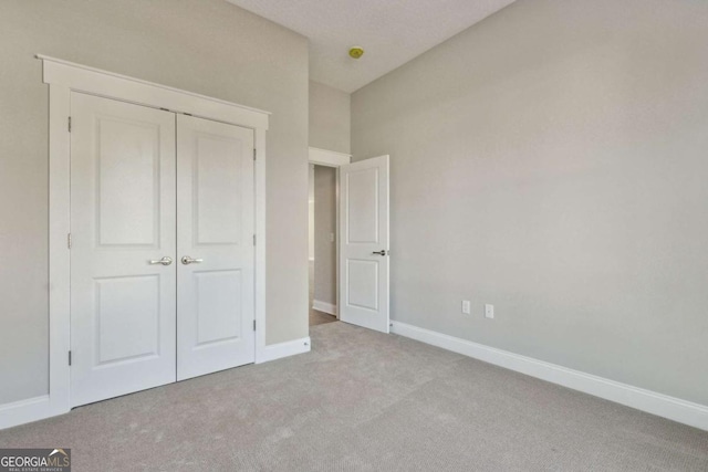 unfurnished bedroom featuring baseboards, a closet, and light colored carpet