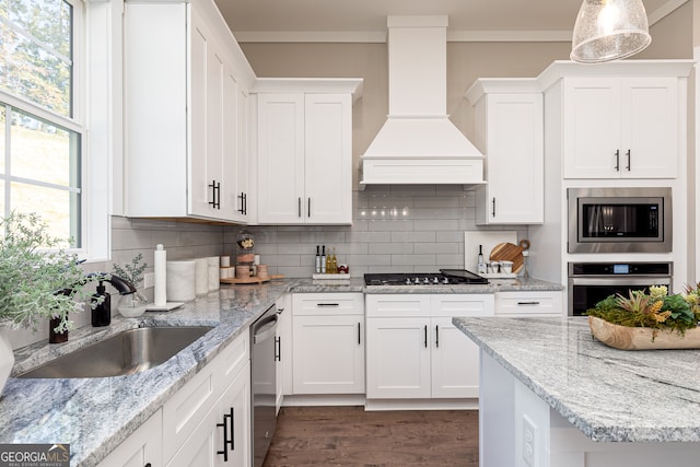 kitchen featuring decorative light fixtures, custom range hood, appliances with stainless steel finishes, white cabinetry, and a sink