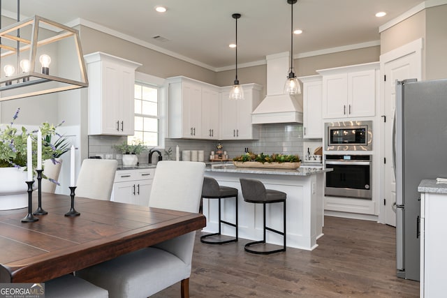 kitchen with premium range hood, a kitchen island, white cabinetry, appliances with stainless steel finishes, and crown molding