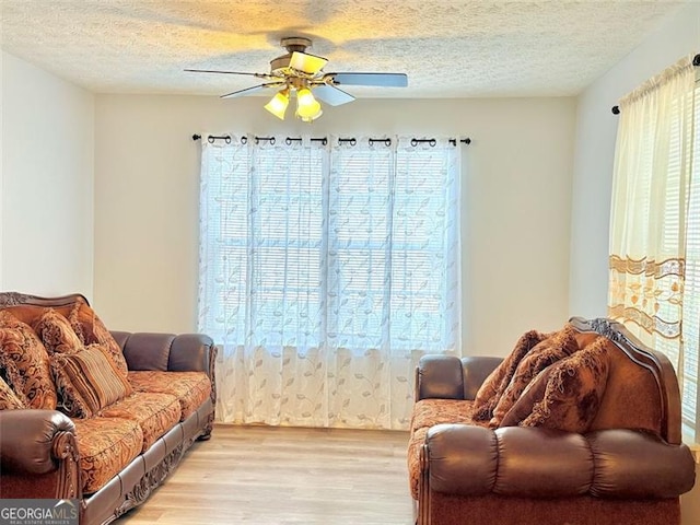 living area with light wood-style flooring, a textured ceiling, and a ceiling fan