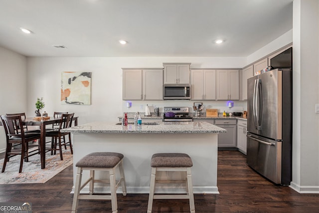 kitchen featuring light stone counters, gray cabinetry, appliances with stainless steel finishes, a sink, and an island with sink