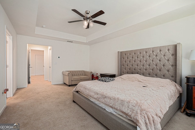 bedroom featuring light carpet, visible vents, a ceiling fan, baseboards, and a tray ceiling