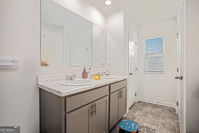 full bathroom featuring stone finish floor, a sink, baseboards, and double vanity