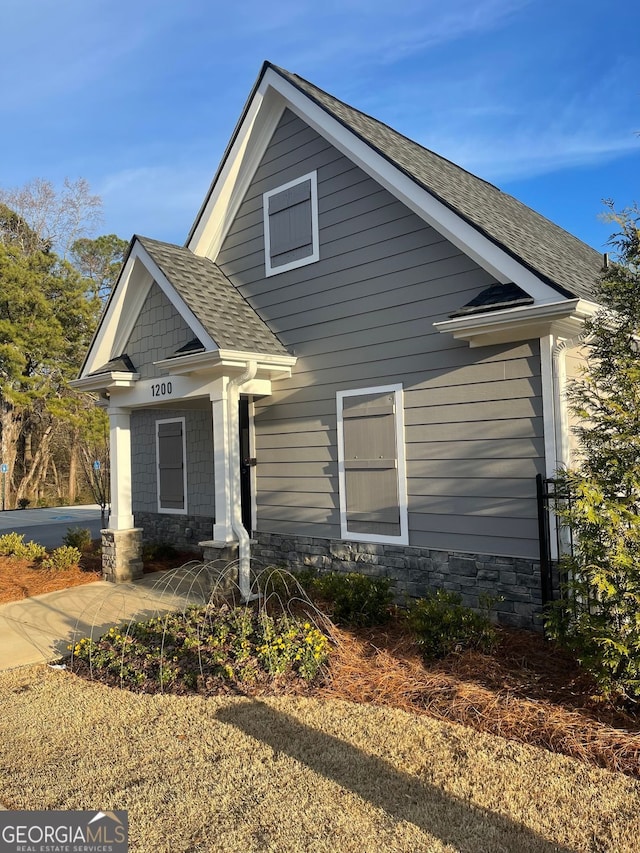 view of front of property featuring stone siding and roof with shingles