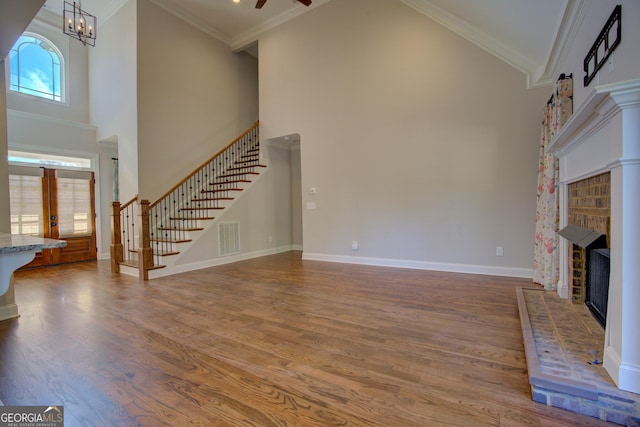 unfurnished living room featuring a fireplace, visible vents, stairway, ornamental molding, and wood finished floors