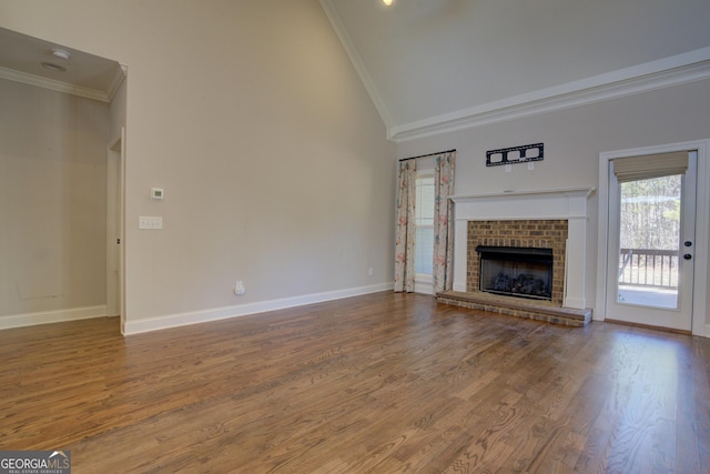 unfurnished living room with baseboards, wood finished floors, crown molding, a brick fireplace, and high vaulted ceiling