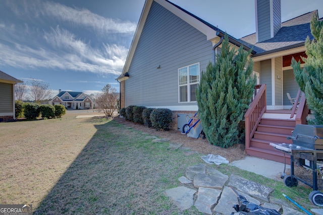 view of side of property with a shingled roof, a chimney, and a lawn