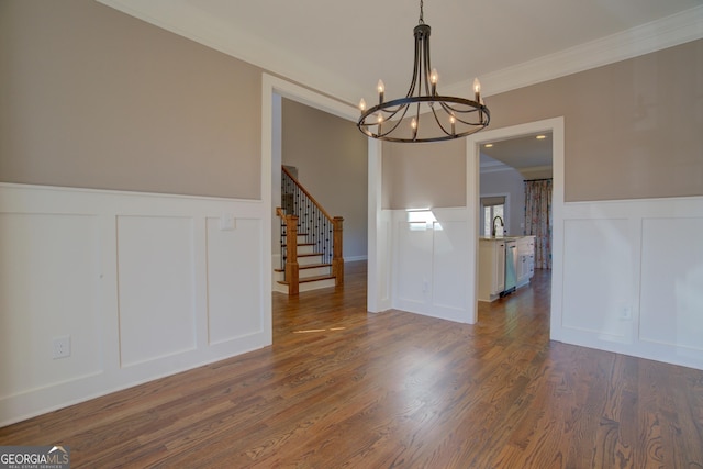 unfurnished dining area featuring a wainscoted wall, a decorative wall, dark wood-type flooring, ornamental molding, and stairs