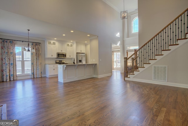 unfurnished living room featuring dark wood finished floors, visible vents, stairway, ornamental molding, and a chandelier