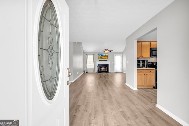 interior space featuring light wood-type flooring, a fireplace, baseboards, and a ceiling fan