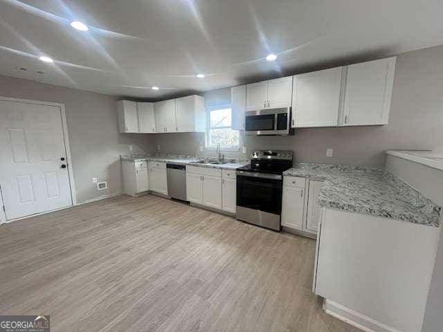 kitchen featuring light wood finished floors, appliances with stainless steel finishes, white cabinetry, a sink, and light stone countertops