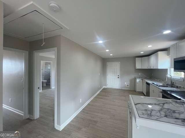 kitchen featuring appliances with stainless steel finishes, light wood-style floors, white cabinets, a sink, and baseboards